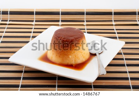 Close-up of a vanilla cream and caramel dessert with spoon on white dish