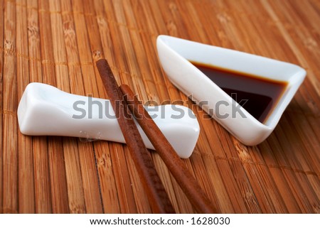 A pair of asian chopsticks and soy sauce, over the bamboo mat