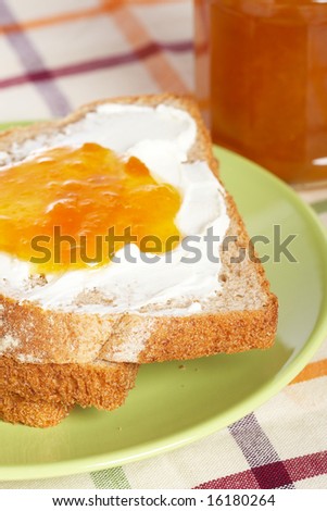 Toast with butter and peach jam glass jar in the green plate with soft shadow on square mat background. Shallow depth of field