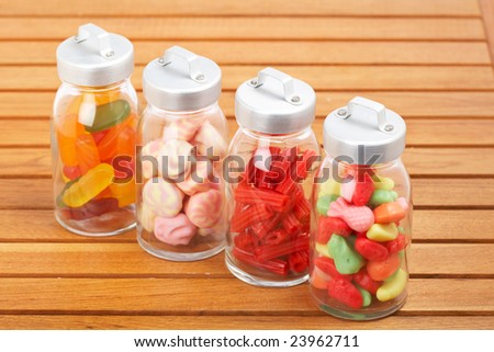 Assortment of glass jars with marshmallows, candies and red licorice on wooden background. Shallow depth of field