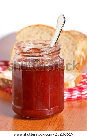Strawberry jam glass jar and bread on square mat. Shallow depth of field