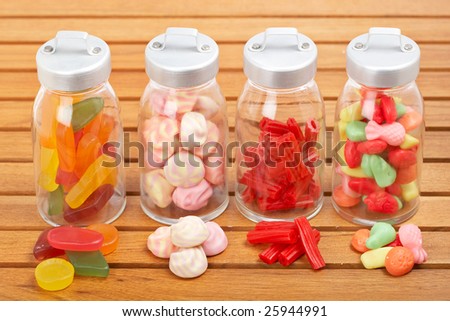 Assortment of glass jars with marshmallows, candies and red licorice on wooden background. Shallow depth of field