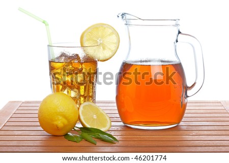 Ice tea pitcher and tumbler with lemon and icecubes on wooden background