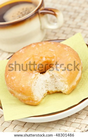 A coffee and bitten donut with shallow depth of field