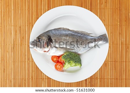 Fresh fish with broccoli and cherry tomatoes in the white plate on on bamboo mat