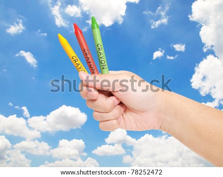 Hands holding color pencils and crayons against blue sky against blue sky