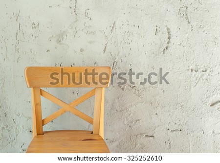Wooden chair with a backrest in natural light. Background rough white plaster.