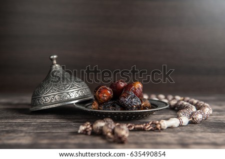 Date-palm is placed on silver. date palm fruits or kurma, ramadan on a wooden black background.