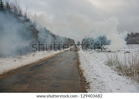Scenic view of road receding through snowy countryside with smoke from fire.