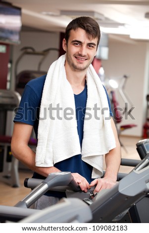 young man training in the gym, smiling, with towel around his neck