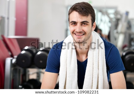 young man training in the gym, smiling, seated, with towel around his neck