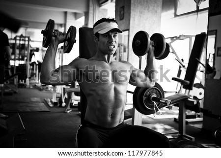 artistic shot, black and white, of a young bodybuilder hard training in the gym: dumbbell shoulder press