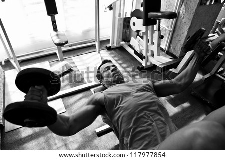 artistic shot, black and white, of a young bodybuilder hard training in the gym: incline dumbbell press