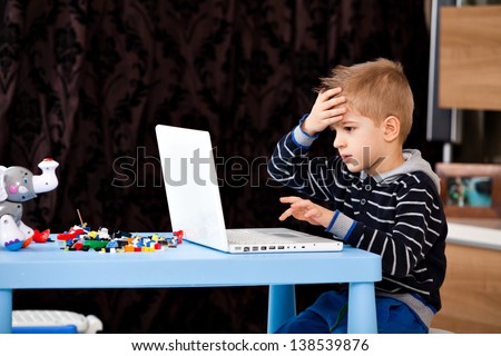 a five years old child looking at his laptop at home, kid playing at laptop in the living room, making a mistake, failure, losing