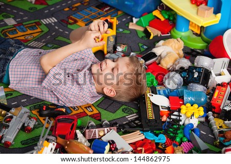A five year old child playing in his room with a lot of toys around him