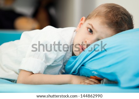 A sad five year old child sitting in his bed with his head on a blue pillow