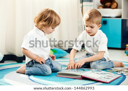 A five year old child and his two year old brother playing in their room. A five year old child showing his two year old brother the pictures from a book