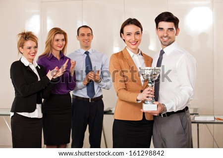 young couple holding a trophy; happy business people celebrating their victory, applauded by their partners
