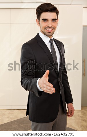 portrait of a young handsome business man smiling inviting to a handshake, focus on the face