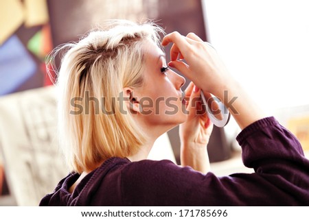 beautiful blonde woman applying false lashes to herself