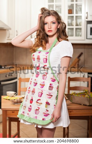 Beautiful sexy caucasian woman wearing an apron and elegantly posing standing in the kitchen with a hand in her hair