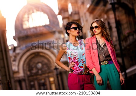 Fashion shot of two elegant beautiful girls in the sunset wearing sunglasses. Two young women outdoor on the street. Shopping inspiration