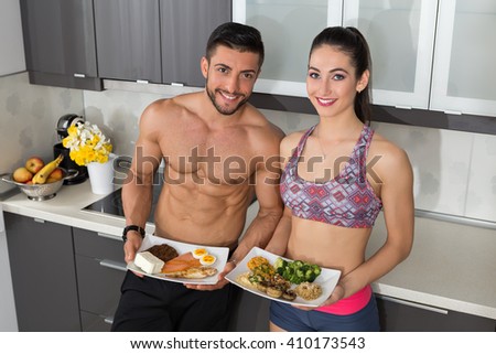 fit couple in the kitchen; animal versus plant proteins: one plate with beef, eggs, salmon, cheese and chicken grill and another with nuts, mushrooms, broccoli, lentil, hummus and quinoa