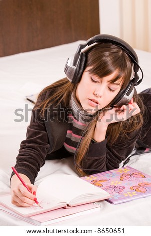 Teenage girl writing in her diary an listening to music in professional earphones