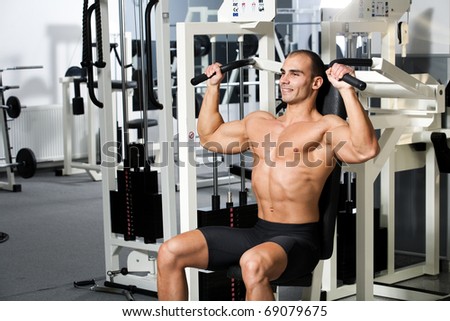 young bodybuilder training in the gym - machine shoulder press, start position