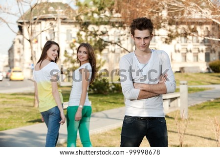 two young women looking at a young man, in the park