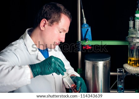 Scientist working in lab Male wearing white lab coat and green plastic gloves holding glassware