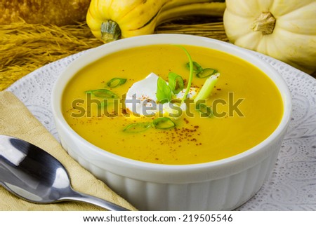 Close up of yellow squash soup with a dollop of sour cream and scallions, sprinkled with paprika