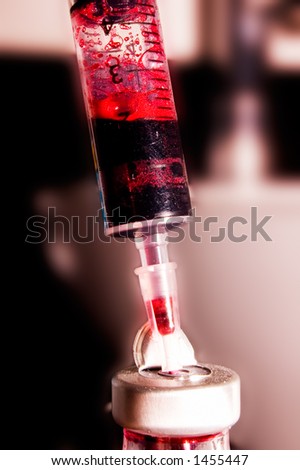 Needle with red liquid stuck in a bottle.