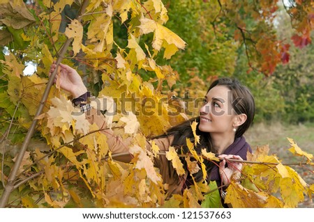 young woman looks through yellow autumn leaves