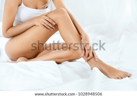 Long Woman Legs With Smooth Soft Skin. Close Up Of Female With Perfect Healthy Silky Legs Skin After Hair Removal On White Bed In Light Interior. Beauty, Skin Care Concept. High Resolution.
