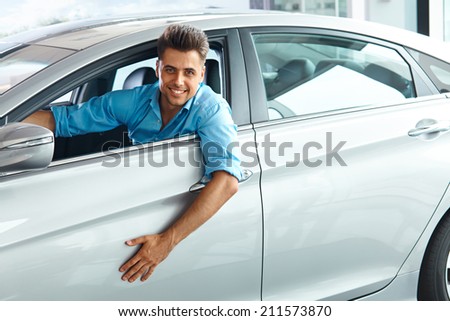 Car Showroom. Happy Man inside Car of His Dream.