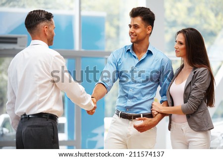 Car Showroom. Young Couple is Meeting with Seller in Auto Salon