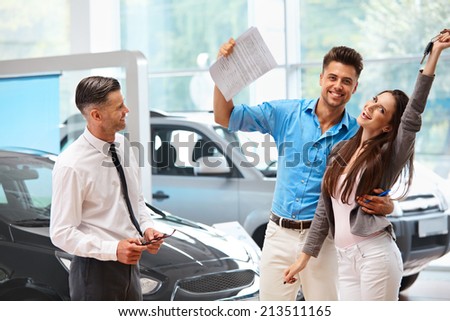 Young Couple Celebrating Purchase of a car In Car Showroom
