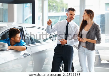 Car Salesman Giving a Key From the New Car to the Young Owners