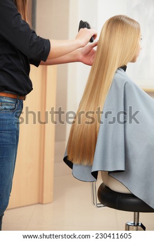 Blonde hair. Hairdresser combing long blonde hair in salon
