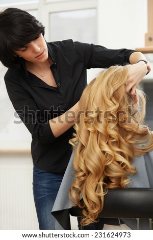 Blonde curly hair. Hairdresser doing hairstyle for young woman in salon