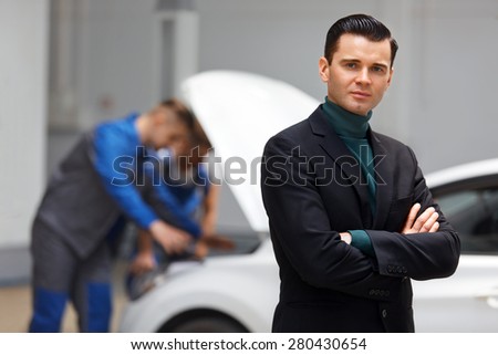 Portrait of Happy Customer in Auto Repair Shop With Mechanics in Background