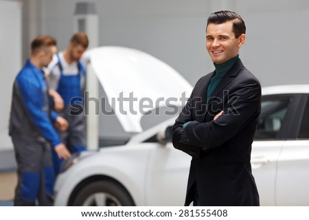 Portrait of Happy Customer in Auto Repair Shop With Mechanics in Background