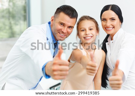 Dentist doctor,  assistant and little girl all smiling at camera with thumbs up at the dental clinic