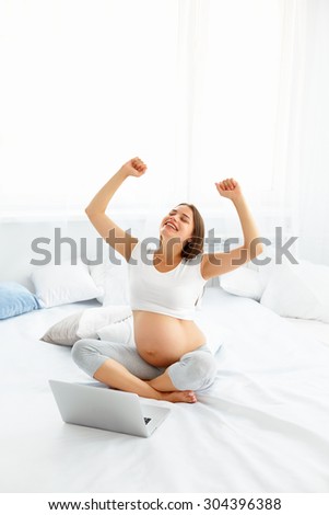 Pregnant Woman Celebrates Something. Happy Woman using Laptop Computer. Online Shopping