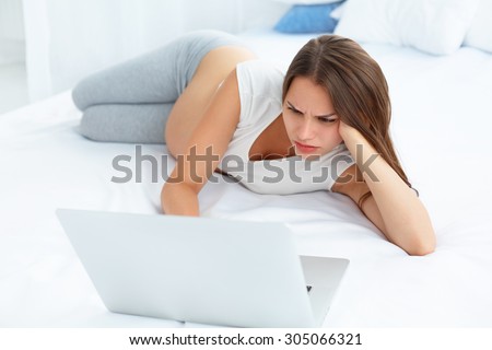 Depressed Pregnant Woman Works at Laptop Computer While Lying on a Bed