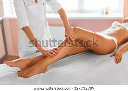 Spa treatment. Body care. Massage of human legs in spa salon. Close-up of masseur applying moisturizing oil and massaging beautiful long tanned female legs. Skin care, wellness concept.