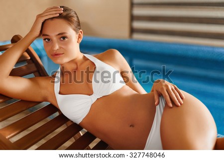 Body woman care. Beautiful girl with sexy body in elegant white bikini relaxing  on the deckchair  beside a swimming pool  in resort spa hotel. Spa, sauna, skin care, wellness, concept.