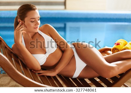 Body care.  Woman with perfect slim body  in white bikini lying on the deckchair by swimming pool in resort spa hotel. Spa, sauna, skin care, lifestyle, wellness, wellbeing concept.
