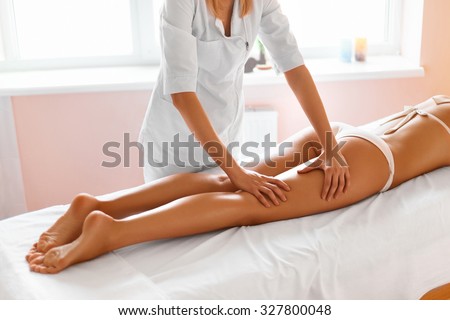 Body care. Close-up of beautiful long tanned woman legs receiving massage in spa salon. Skin care, wellbeing, wellness concept. Anti-cellulite spa treatment.